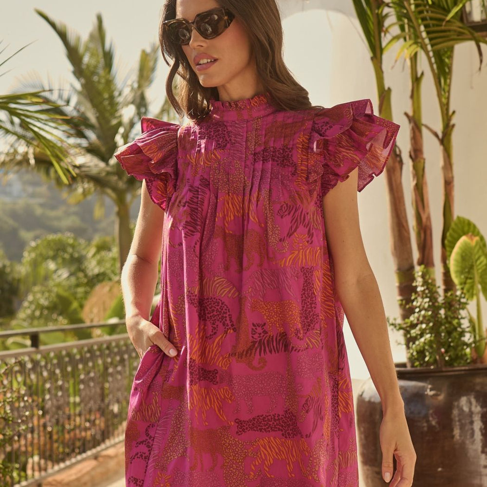 Woman wearing a pink dress with ruffled sleeves in an outdoor setting with plants and mountains.