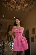 Woman in a pink dress standing in an elegant interior setting with a chandelier.