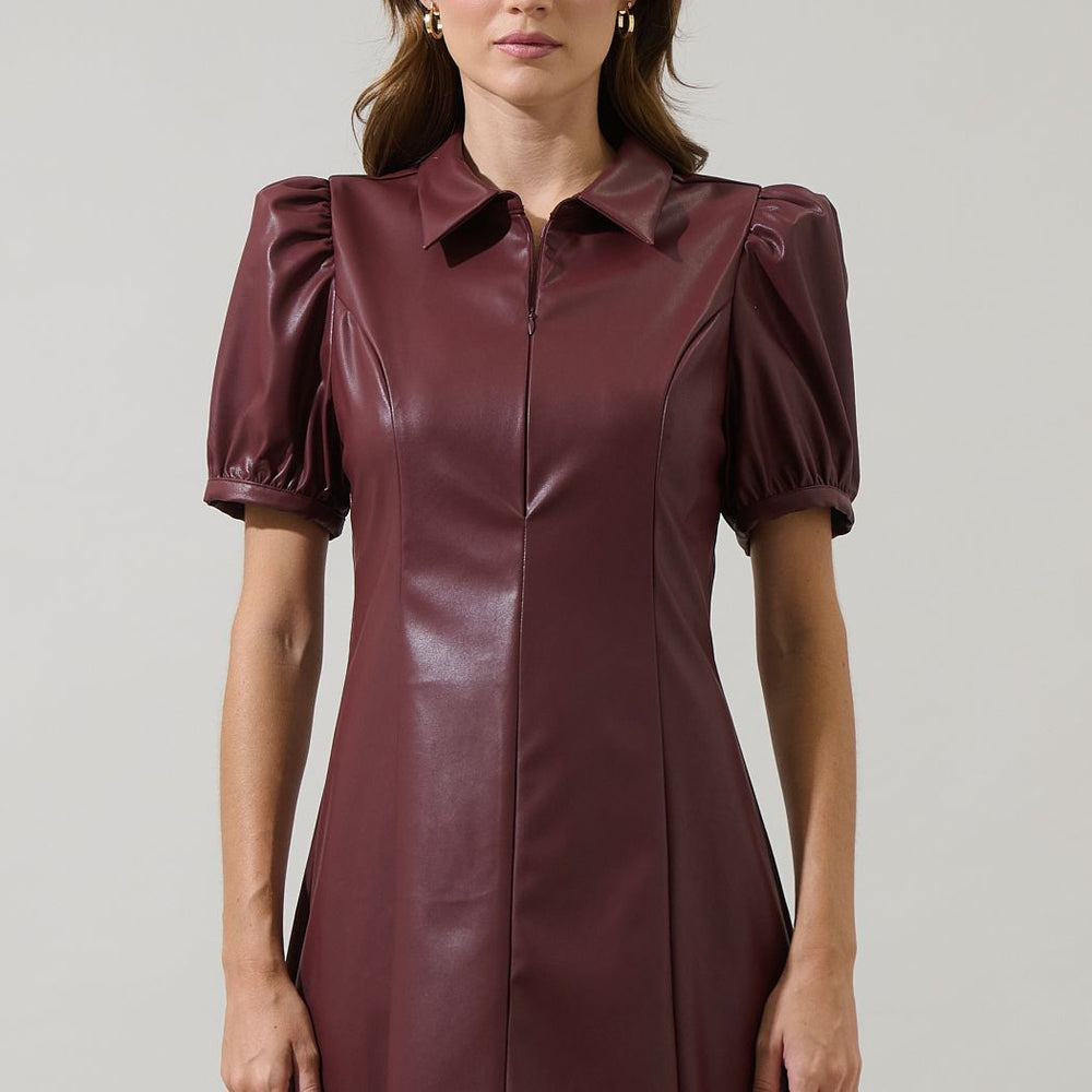 Woman wearing a burgundy leather dress with puff sleeves on a plain background