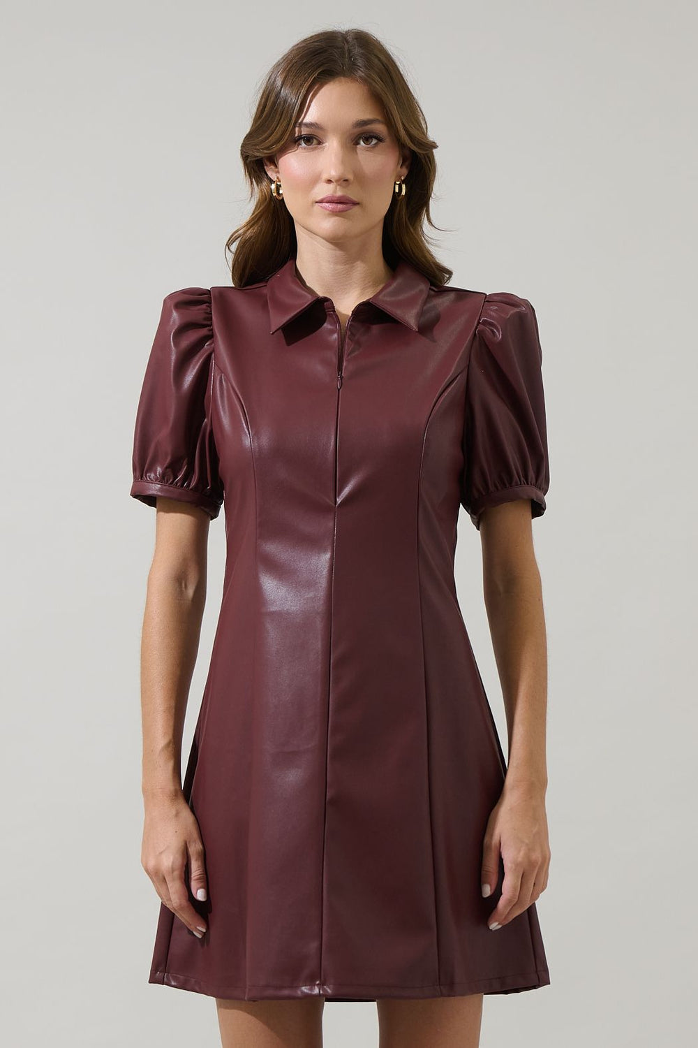 Woman wearing a burgundy leather dress with puff sleeves on a plain background
