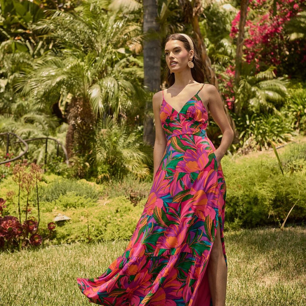 Woman in a colorful dress standing in a garden with lush greenery and flowers.

