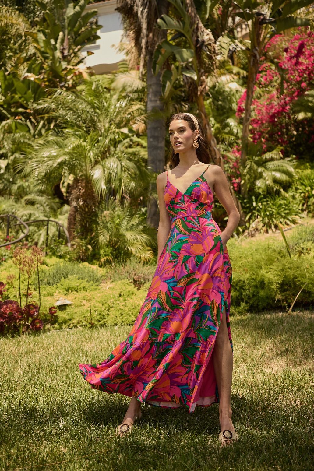 Woman in a colorful dress standing in a garden with lush greenery and flowers.

